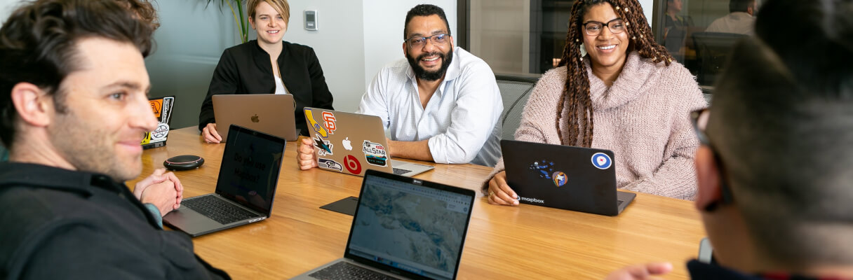 Equipe diversa em uma reunião colaborativa com laptops em uma sala de conferências.